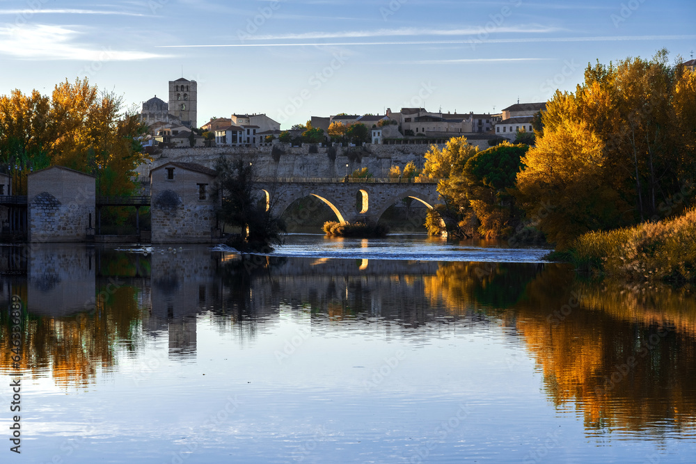 View of the city of Zamora and watermills and the romanesque cathedral in autmn at sunset reflected in the Duero river. Spain - obrazy, fototapety, plakaty 