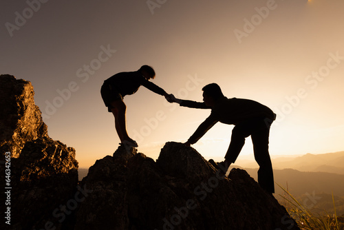 Silhouettes of two people climbing on mountain and helping. Help and assistance concept. Helping hand, Sports training.