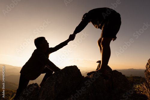 Silhouettes of two people climbing on mountain and helping. Help and assistance concept. Silhouette of Teamwork on the mountains Helping hand, Sports training.