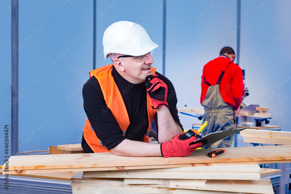 Furniture shop worker. Carpenter man thought. Carpentry worker. Guy in white protective helmet. Man makes career in furniture shop. Carpenter in reflective vest. Carpenter smiles and looks away Furniture shop worker. Carpenter man thought. Carpentry worker. Guy in white protective helmet. Man makes career in furniture shop. Carpenter in reflective vest. Carpenter smiles and looks away
