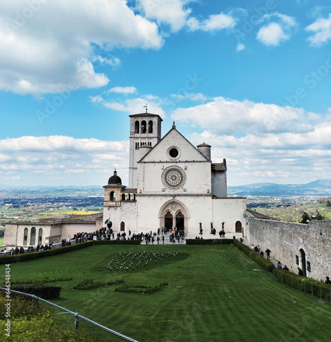 A captivating frontal view of the stunning Basilica of San Francesco in Assisi, Italy. The imposing architecture stands proudly against a dramatic cloudy sky, creating a scene of timeless beauty.