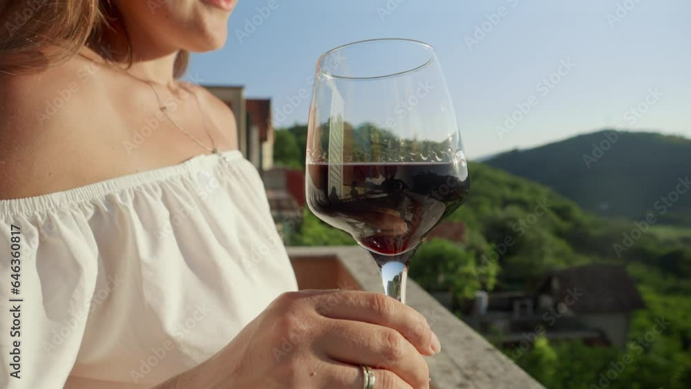 Young woman with glass of red wine gracefully held, merges with the magic of a mesmerizing sunset and mountain view from the villa balcony or terrace. Travel, summertime, and holiday serenity. Young woman with glass of red wine gracefully held, merges with the magic of a mesmerizing sunset and mountain view from the villa balcony or terrace. Travel, summertime, and holiday serenity.