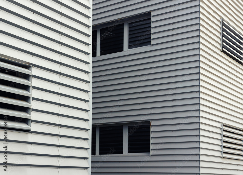 A close-up of a minimalist and modern building facade, showcasing the interplay of sleek gray panels and smooth rectangular windows. Selective focus. A close-up of a minimalist and modern building facade, showcasing the interplay of sleek gray panels and smooth rectangular windows. Selective focus.