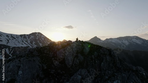 Female artist paints the picture on canvas on sunset on the peak of mountain, aerial view opening shot, fly over the girl. photo