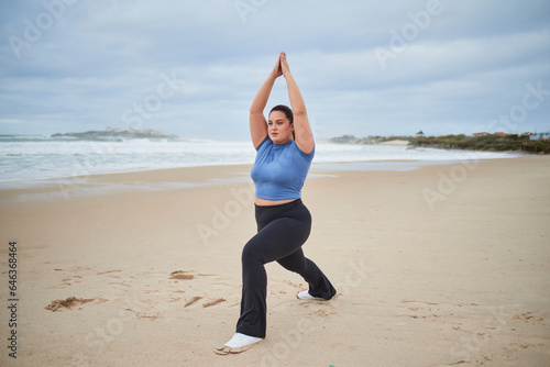Enthusiastic plus size woman raising hands and exercising at the cloudy sea beach