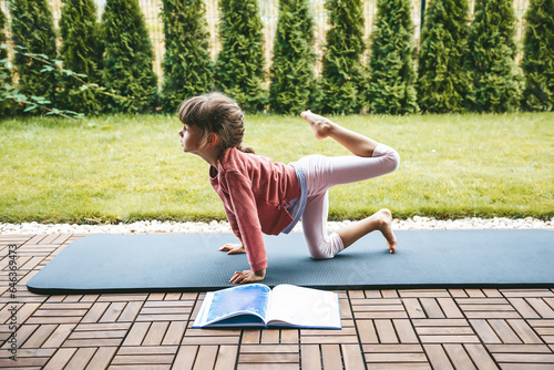 Little girl 5-6 years old stretching in Tiger Pose, or Vyaghrasana on the roll mat practicing yoga outdoors