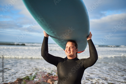 Cheerful overweight female surfer holding surf board at the head and posing