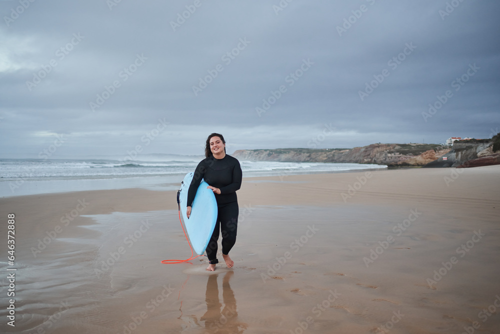 Happy european body positive girl on her way to the ocean with surfboard Happy european body positive girl on her way to the ocean with surfboard