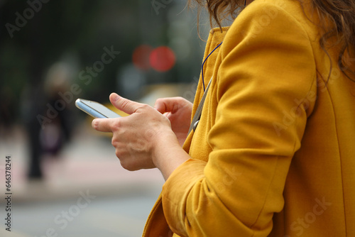 Woman standing with smartphone on a street on traffic lights background. Mobile communication in autumn city
