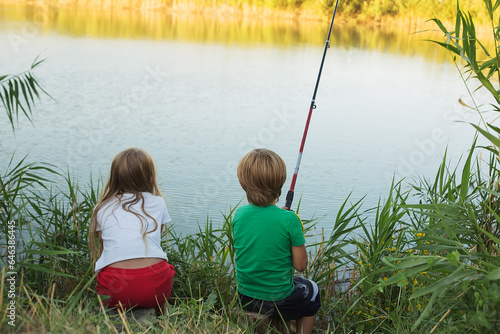 a blonde girl and a boy with a fishing rod in their hands are sitting on the bank of the river fishing