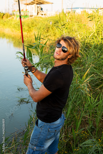 a young man in a black T-shirt and glasses with a cigarette fishing on the river