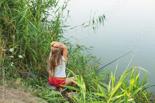 a blonde girl with a fishing rod in her hands is sitting on the bank of the river fishing © Тамара Киреева
