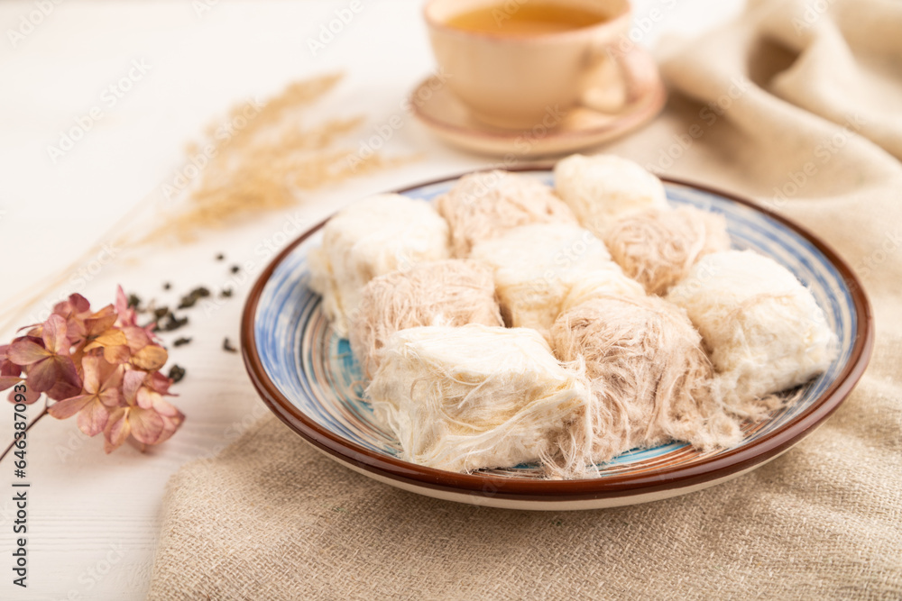 traditional arabic sweets pishmanie and a cup of green tea on white wooden,  side view, selective focus.