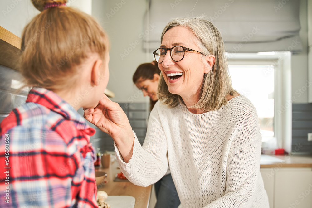 Fototapeta premium Loving grandmother feeding her lovely granddaughter while spending time at the kitchen