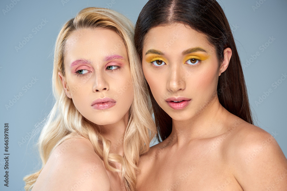 diverse beauty, portrait of two multicultural models with vibrant makeup posing on blue background diverse beauty, portrait of two multicultural models with vibrant makeup posing on blue background