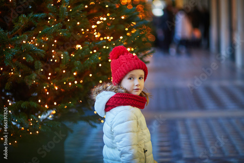 Adorable preschooler girl near Christmas trees decorated with golden baubles in Paris, France