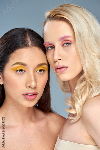 interracial young women with bold eye makeup posing together on blue backdrop  beauty trend concept