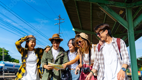 Group of Asian man and woman friends enjoy and fun outdoor lifestyle waiting for train at railway station during travel Thailand on summer holiday vacation. Youth culture and low cost travel concept.