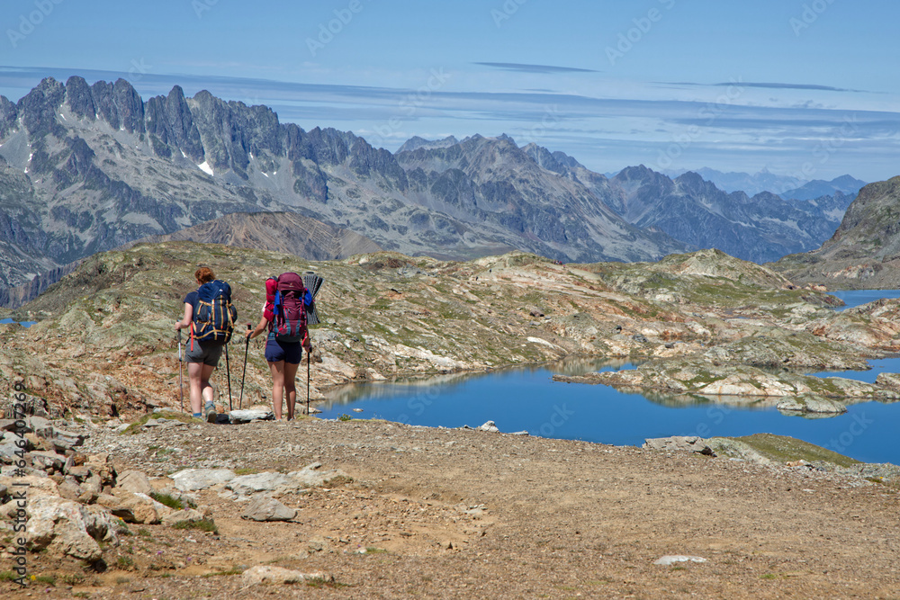 Fototapeta premium OZ-EN-OISANS, FRANCE, August 8, 2023 : Hikers walk on paths over the lakes of Grandes Rousses mountain range