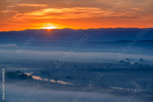 Aerial view of the sunrise over the valley in beautiful early morning mist in the highlands. Low clouds and fog cover the sleeping meadow. Hills valley mists landscape. Serene moment in rural area © Creatikon Studio