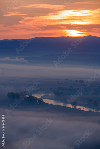 Aerial view of the sunrise over the valley in beautiful early morning mist in the highlands. Low clouds and fog cover the sleeping meadow. Hills valley mists landscape. Serene moment in rural area © Creatikon Studio