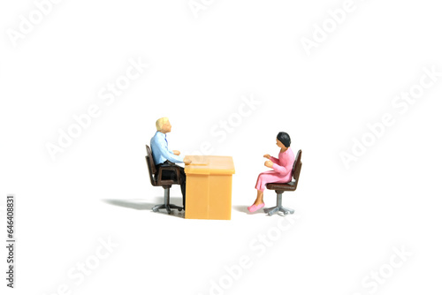 Miniature tiny people toy figure photography. Business conversation concept. A businessman and businesswoman sitting on a chair at office room. Isolated on white background