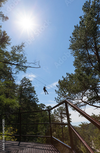 Tourist is going down the ropes - a bungee cable - from a mountain waterfall above the wooded gorge of the Kyngarga River. Fun active summer holiday. Siberia. Buryatia. Arshan resort photo