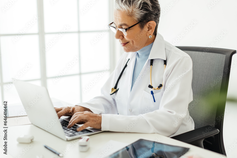 Senior female doctor using medical software on a laptop while working in her office Senior female doctor using medical software on a laptop while working in her office