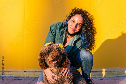 Smiling young woman crouching with water dog in front of yellow wall photo