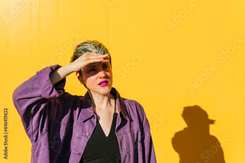 Woman shielding eyes from sunlight in front of yellow wall photo