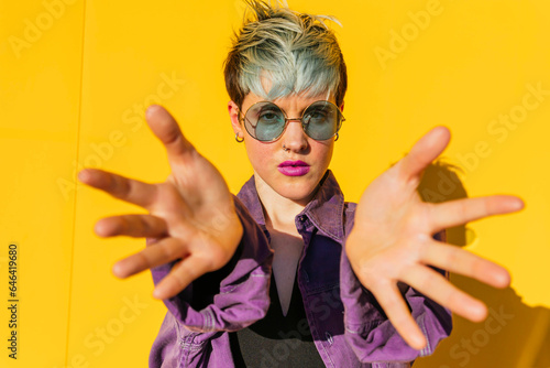 Woman wearing sunglasses showing palms in front of yellow wall photo