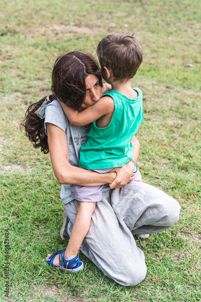 mother and son hugging lovingly on their knees in a green park mother and son hugging lovingly on their knees in a green park