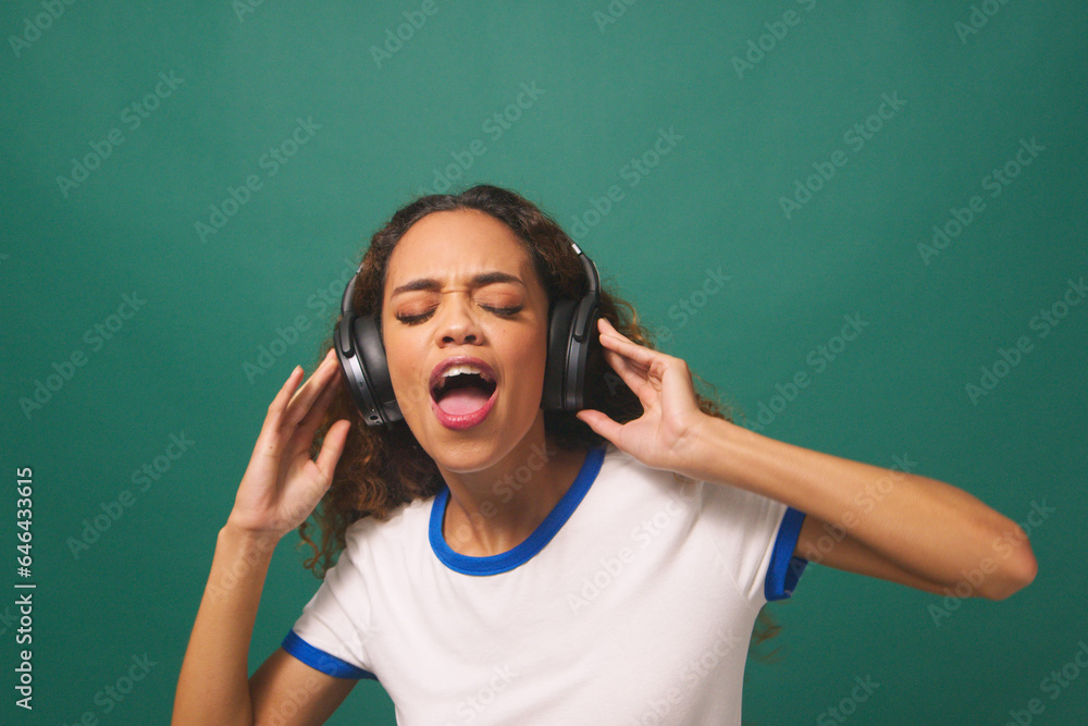 Young biracial woman dancing with headphones, green studio background Young biracial woman dancing with headphones, green studio background