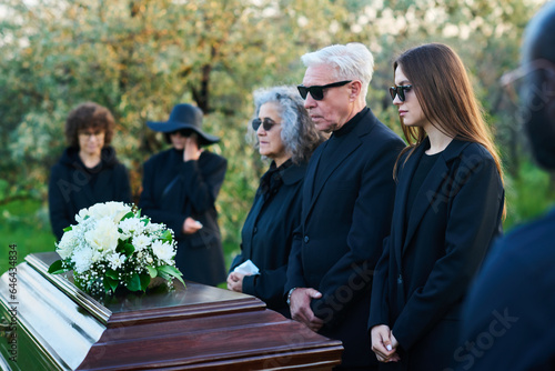 фотографія Family of three grieving people in sunglasses and mourning clothes standing in f