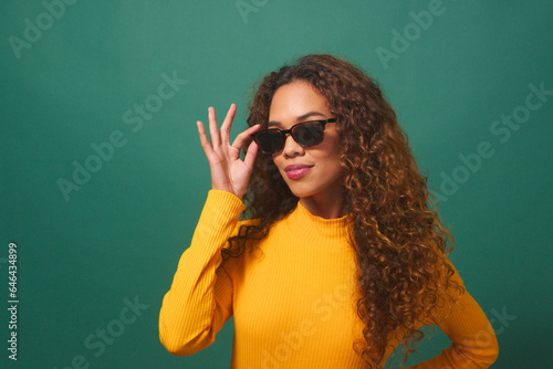 Beautiful young woman cool attitude tips sunglasses, green studio