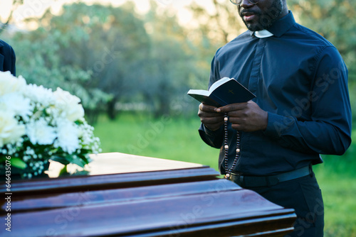 Canvas Print Cropped shot of young priest in black clothes reading verses from Holy Bible dur