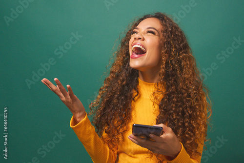 Young biracial woman celebrates after reading text wow, green studio background