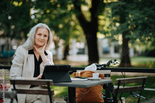 Fotografi Portrait of beautiful female manager in middle age with gray hair working outdoors