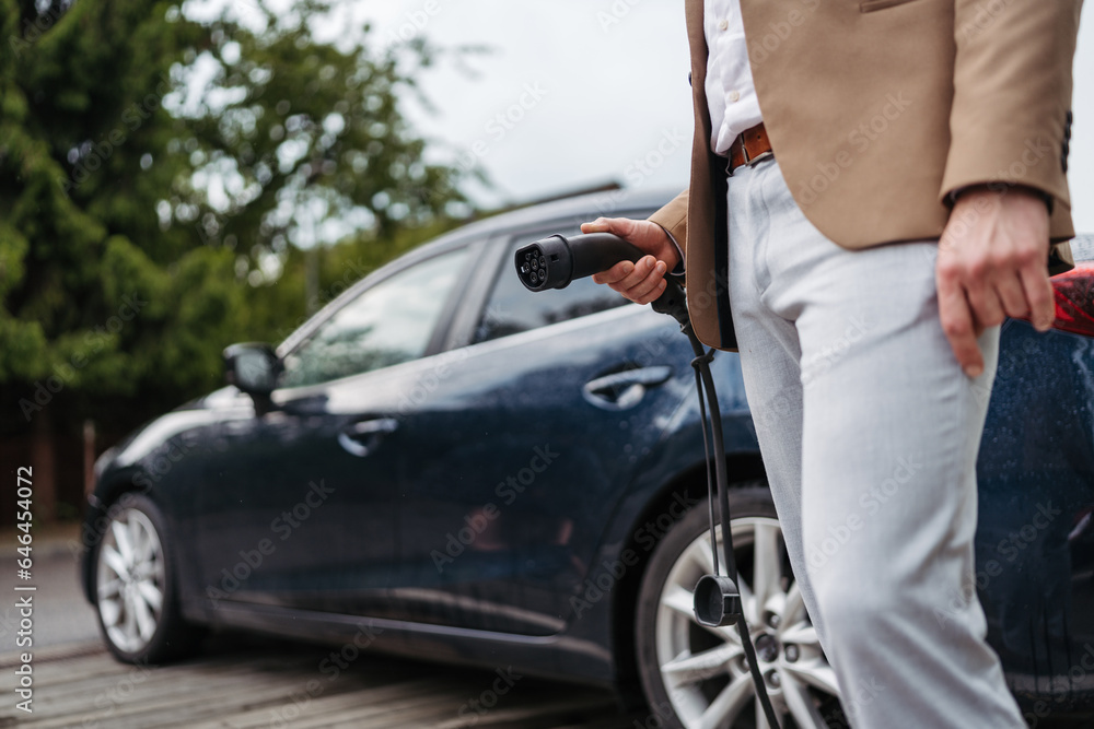 Naklejka premium Close up of a businessman charging electric car.