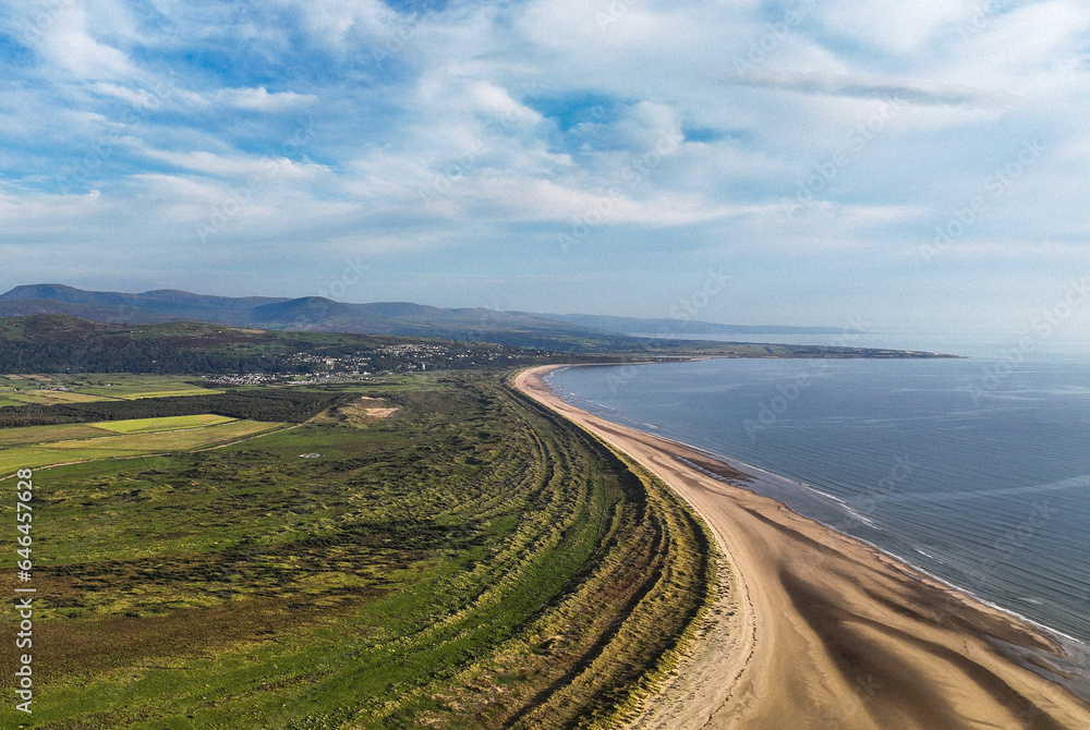 Aerial view of a curved sandy beach against a blue sky and deep blue sea shore coastline
