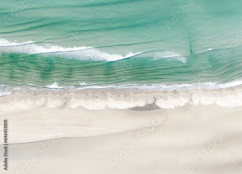 Aeriel birdseye shot of a shoreline in Wales, UK, turqoise sea waves lapping at a sandy beach 