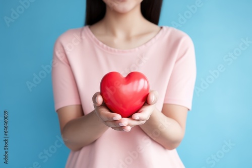 Woman holding a heart symbol against a solid color background - Generosity and Compassion - Loving Care - AI Generated