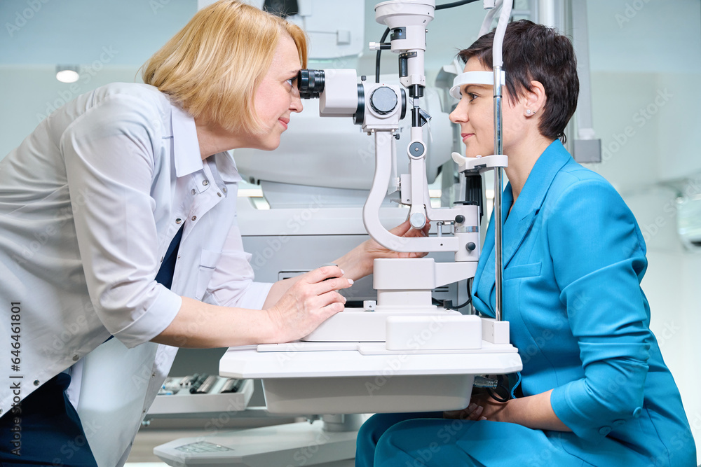 Experienced oculist checking adult woman vision with ophthalmic equipment Experienced oculist checking adult woman vision with ophthalmic equipment