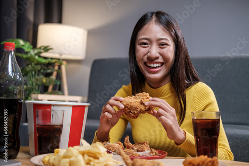 Young Asian woman happily eating fried chicken inside home celebrating the weekend. photo