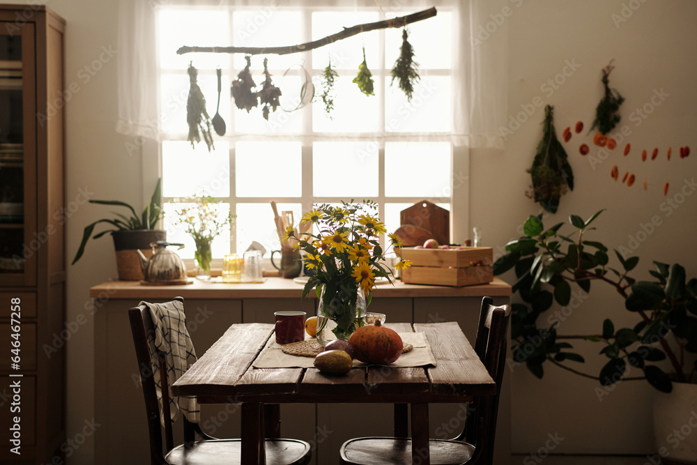 Two wooden chairs standing by table with bunch of yellow garden flowers in vase, ripe pumpkin and eggplants and mug against kitchen counter Two wooden chairs standing by table with bunch of yellow garden flowers in vase, ripe pumpkin and eggplants and mug against kitchen counter