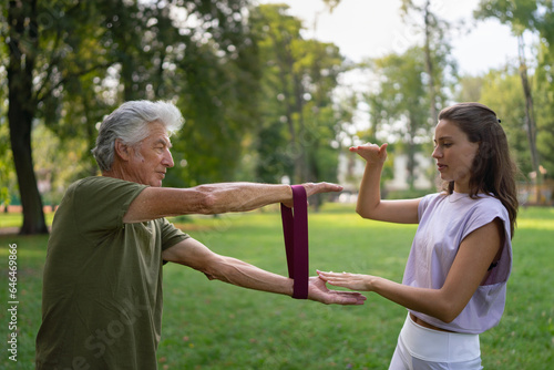 The senior man exercising with physiotherapist or trainer in the park, using resistance band. Elderly healthcare and mental health.  © Halfpoint