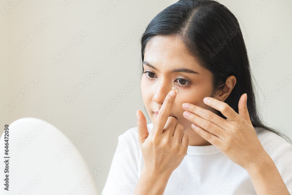 Ophthalmology care, eye sight, vision concept. Asian young woman, female hand holding and putting, wearing soft contact lenses with finger on face, girl looking in mirror at home. Medicine and health. Ophthalmology care, eye sight, vision concept. Asian young woman, female hand holding and putting, wearing soft contact lenses with finger on face, girl looking in mirror at home. Medicine and health.