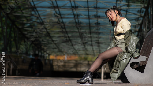 A young Asian woman sits on a bench at the subway exit. 
