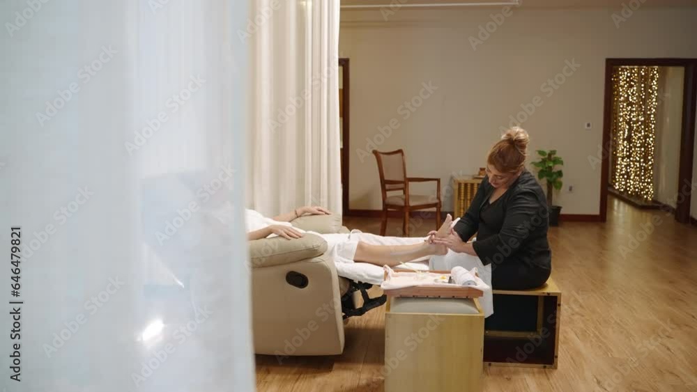 Arabian masseuse doing thai foot massage treatment for customer in spa salon. Young woman getting acupressure relax therapy in arm-chair. Beautician fingers, kneads client foot. Body care center. Arabian masseuse doing thai foot massage treatment for customer in spa salon. Young woman getting acupressure relax therapy in arm-chair. Beautician fingers, kneads client foot. Body care center.