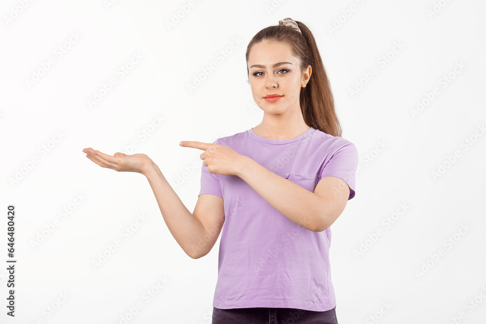 Happy young woman with long hair points finger at banner, shows great promo offer aside, stands in casual t shirt over white background Happy young woman with long hair points finger at banner, shows great promo offer aside, stands in casual t shirt over white background